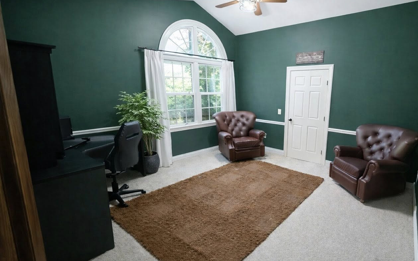 Room with dark green walls, two brown leather armchairs, desk with chair, window, and brown rug.