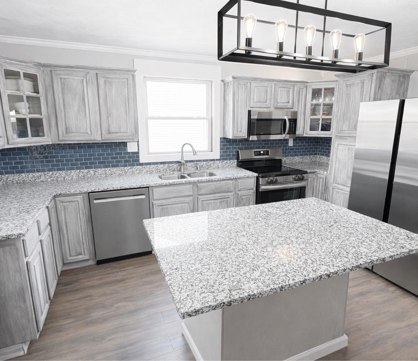 Modern kitchen with gray cabinets, granite countertops, blue tile backsplash, stainless appliances, and island.