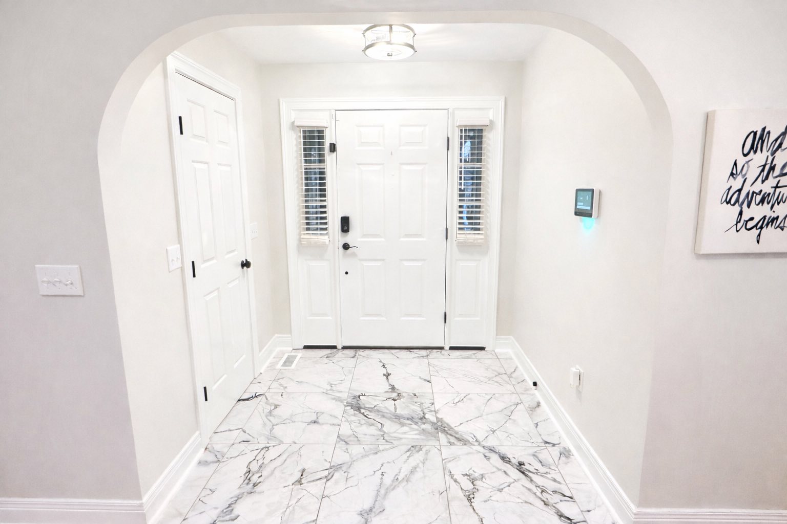 White front door with sidelights, marble tile floor, light gray walls, and a smart home control panel.