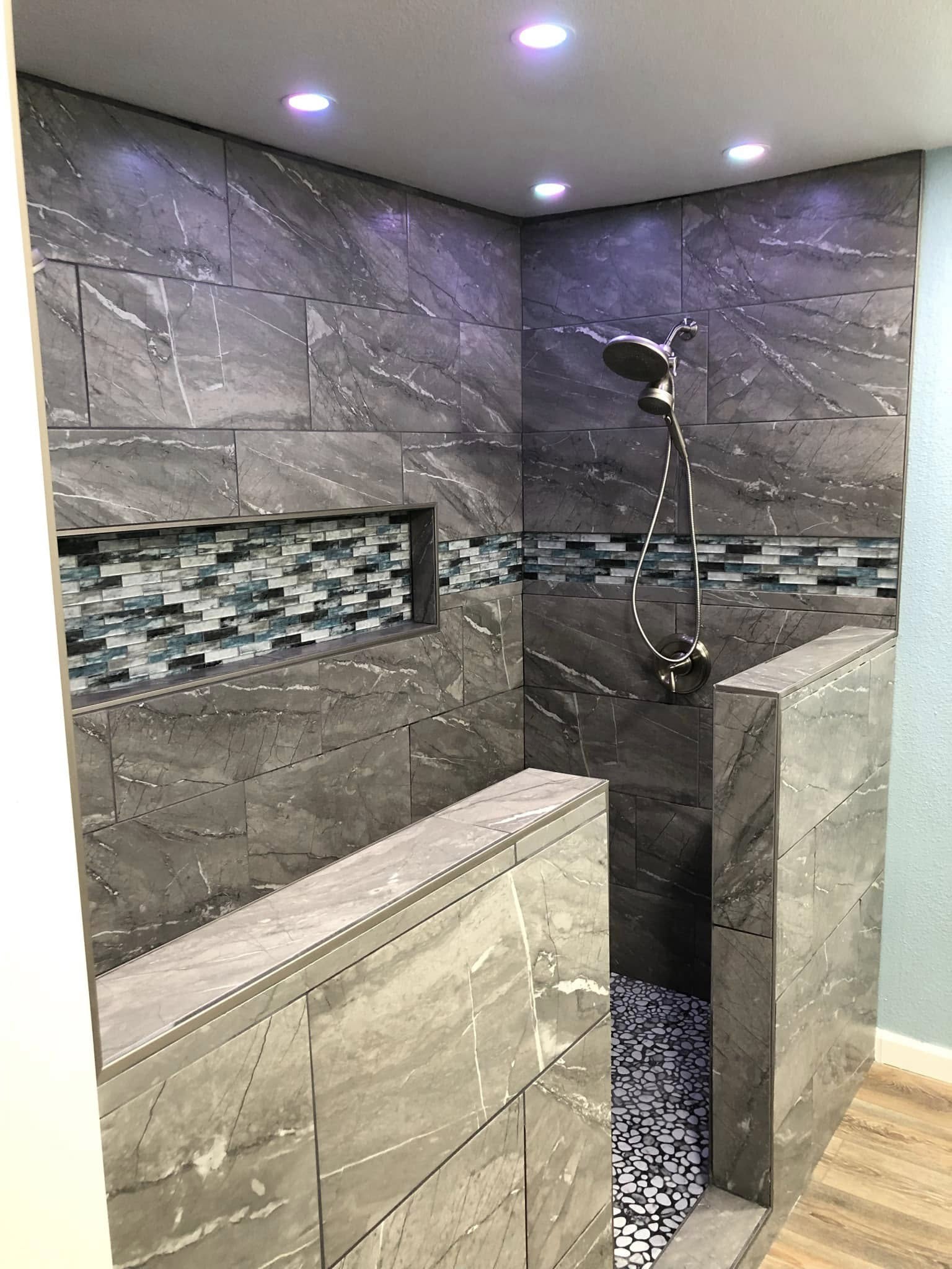 Modern walk-in shower with gray marble tiles, pebble floor, built-in shelf, and overhead showerhead.