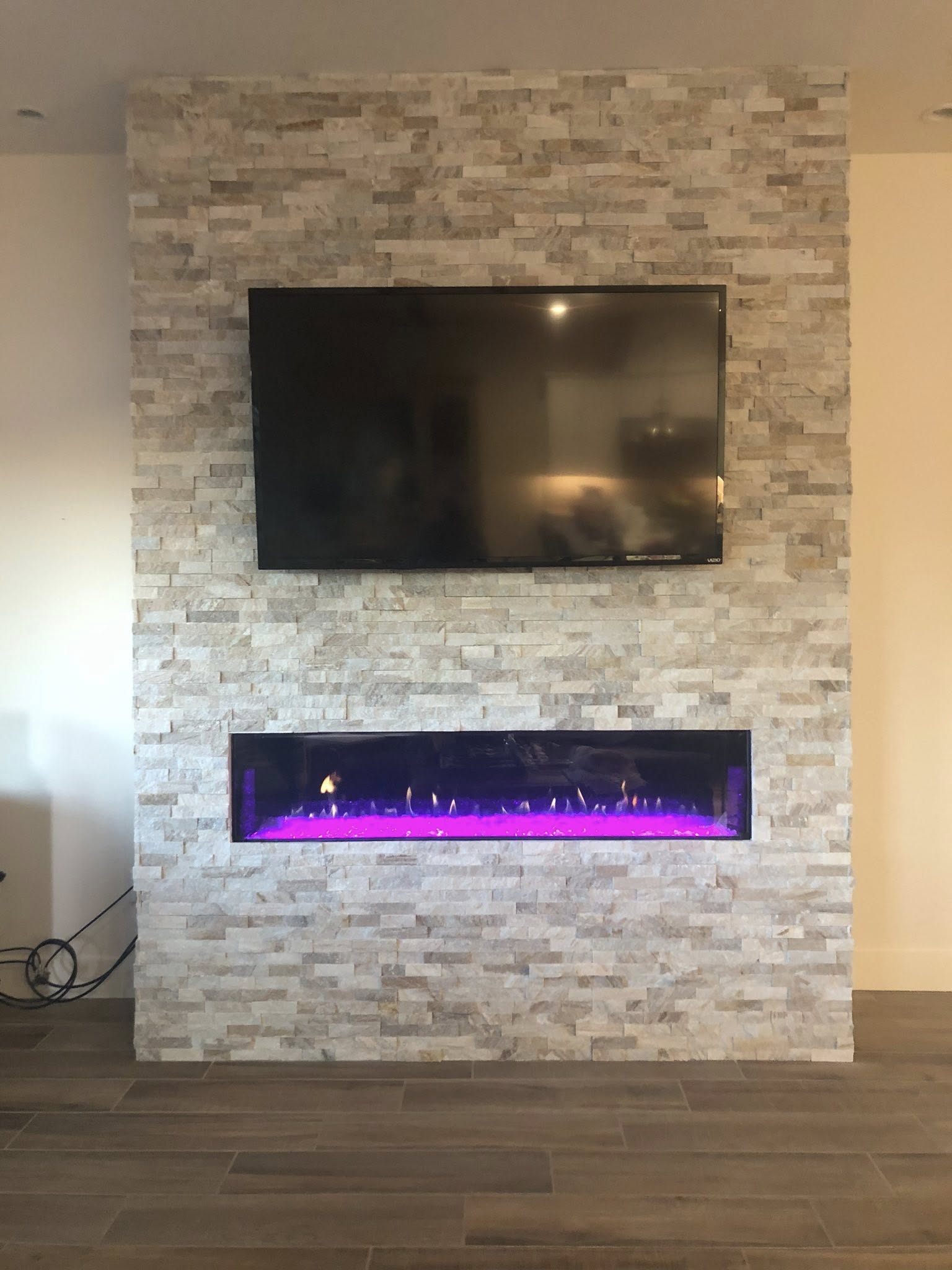 Flat-screen TV mounted above a modern electric fireplace with purple flames on a stone wall.