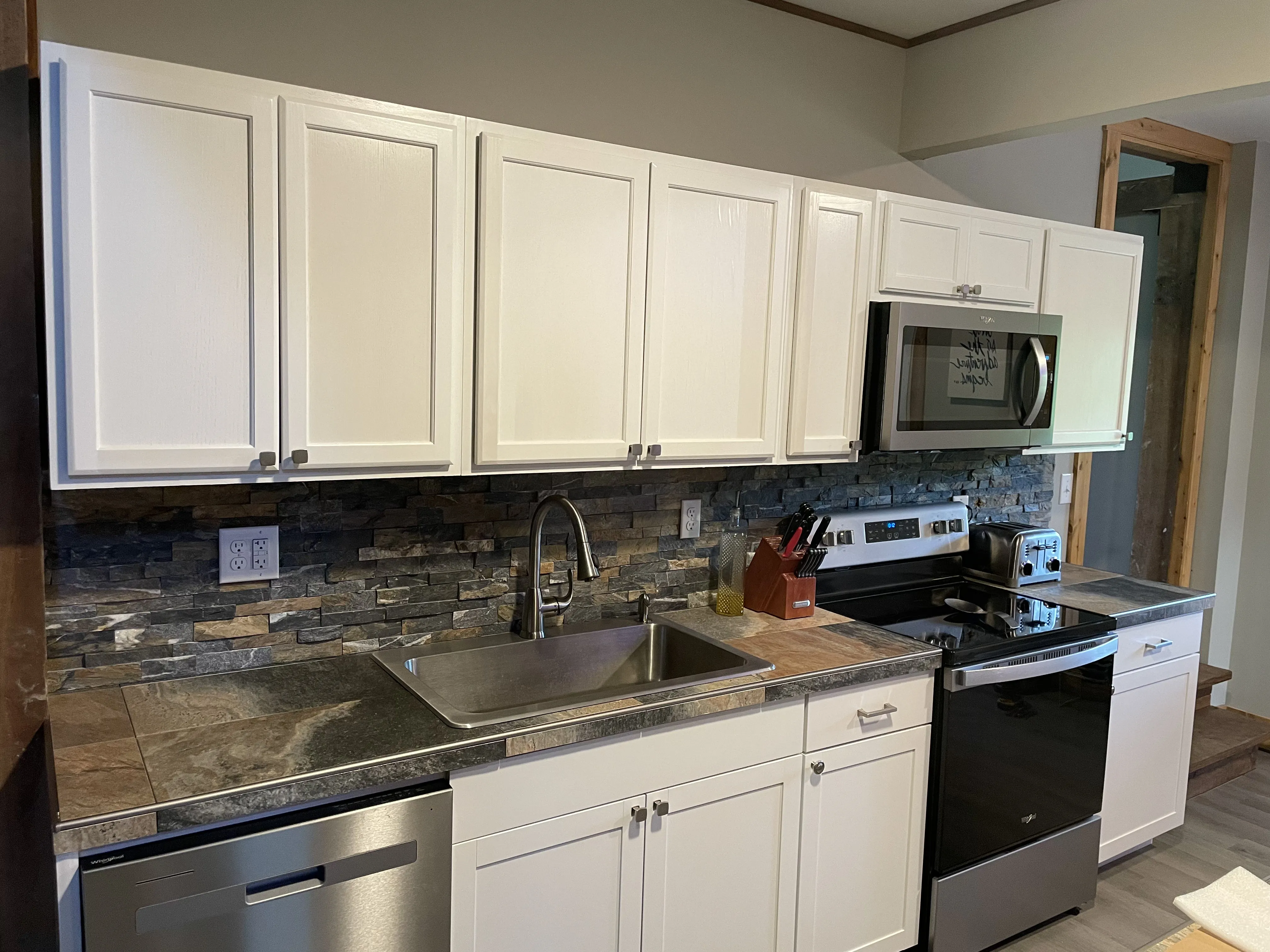 Modern kitchen with white cabinets, stainless steel appliances, stone backsplash, and tiled countertop.