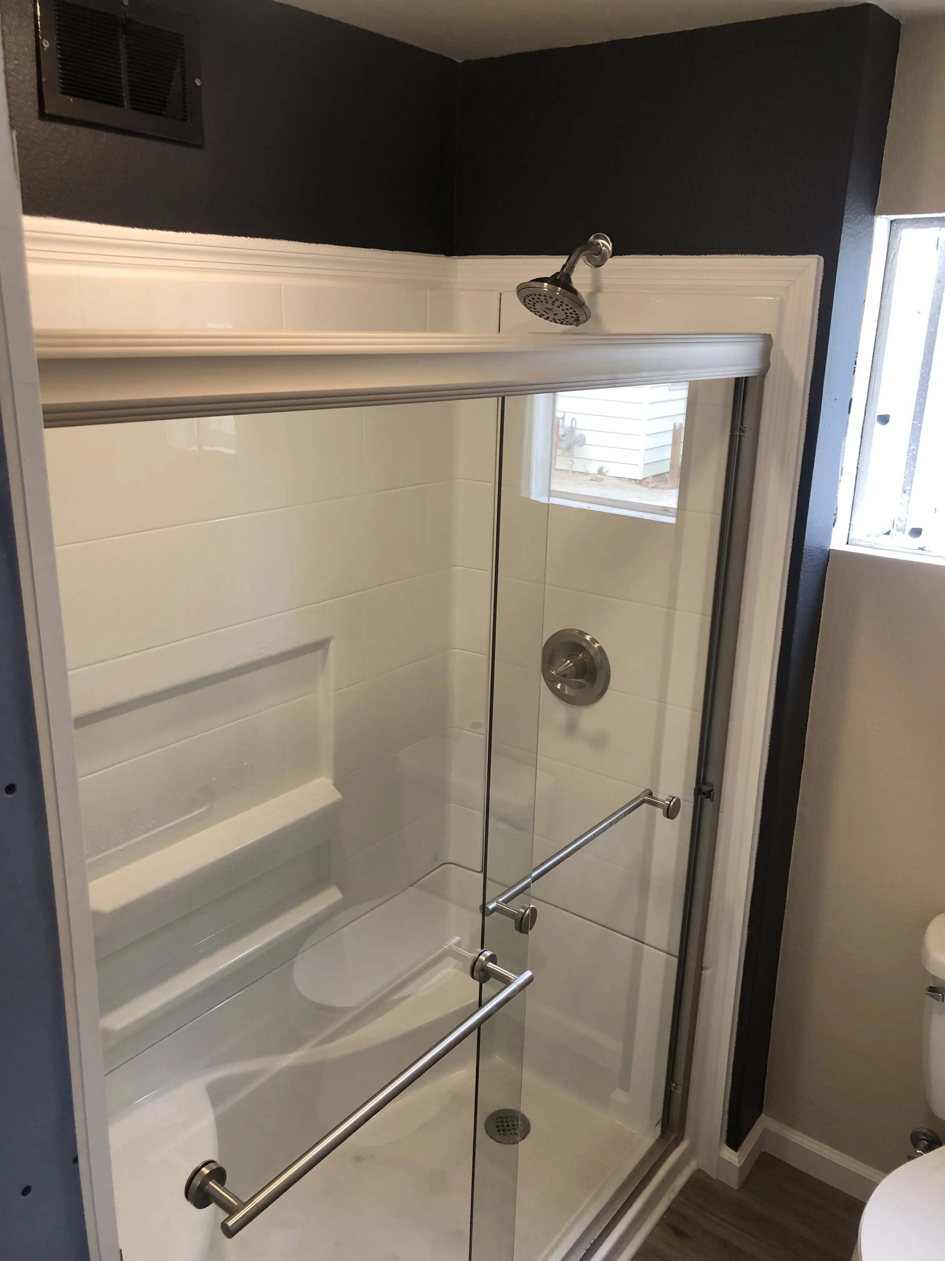Glass shower enclosure with sliding doors, chrome handles, showerhead, and white tiled walls in a bathroom.