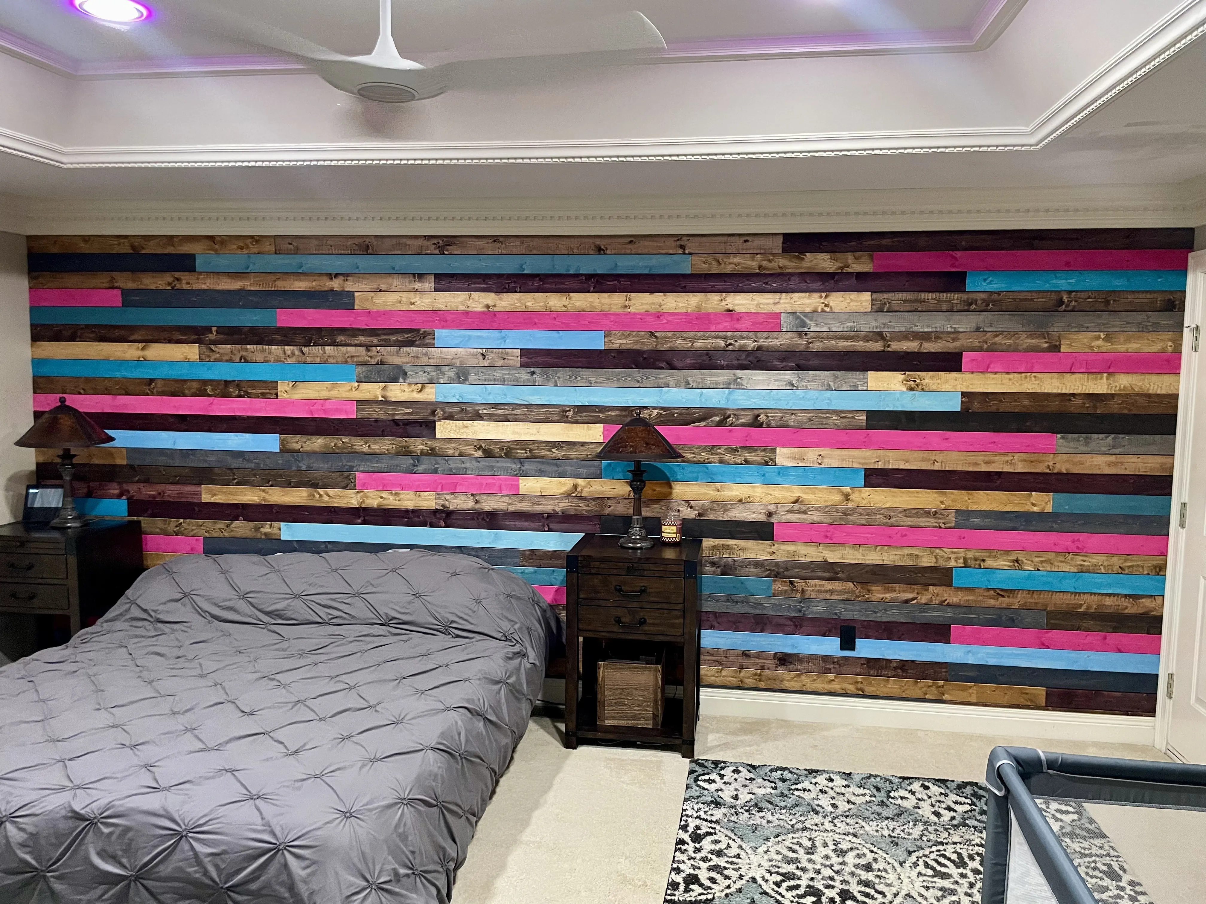Bedroom with multicolored wood plank accent wall, gray bedspread, two wooden nightstands, and patterned rug.