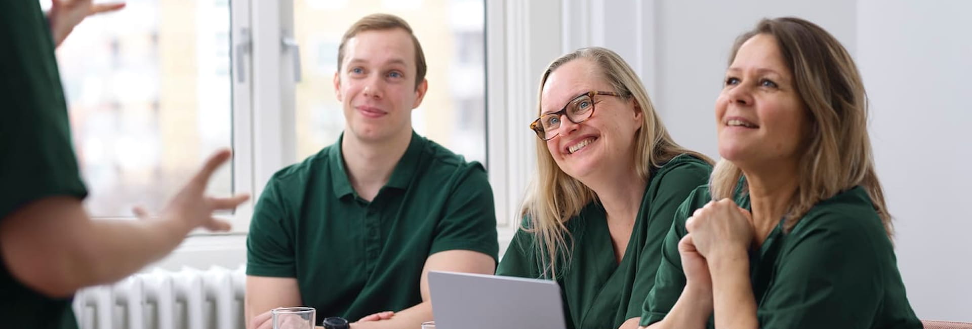 Three practitioners in green scrubs are talking together in front of a whiteboard with notes in a meeting room