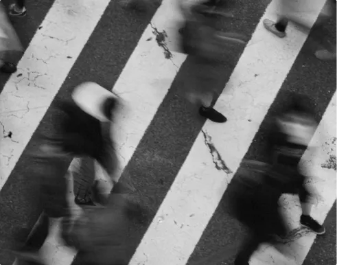Black and white overhead view of blurred pedestrians crossing a street on a zebra crossing.