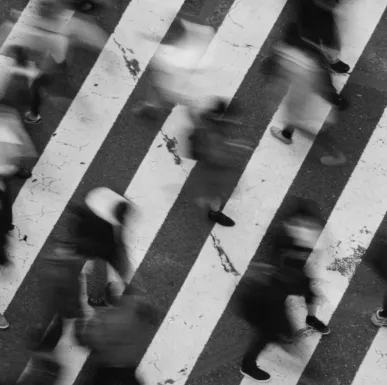 Black and white photo of people walking briskly across a pedestrian crosswalk with motion blur.