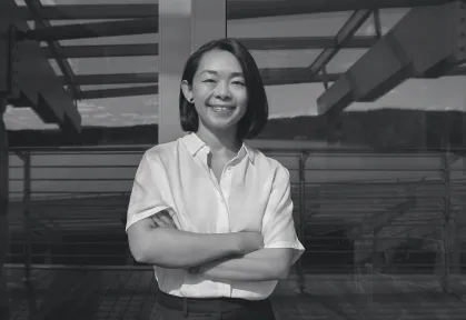 Smiling woman with short hair wearing a white Shirt standing with arms crossed inside a glass-walled building.