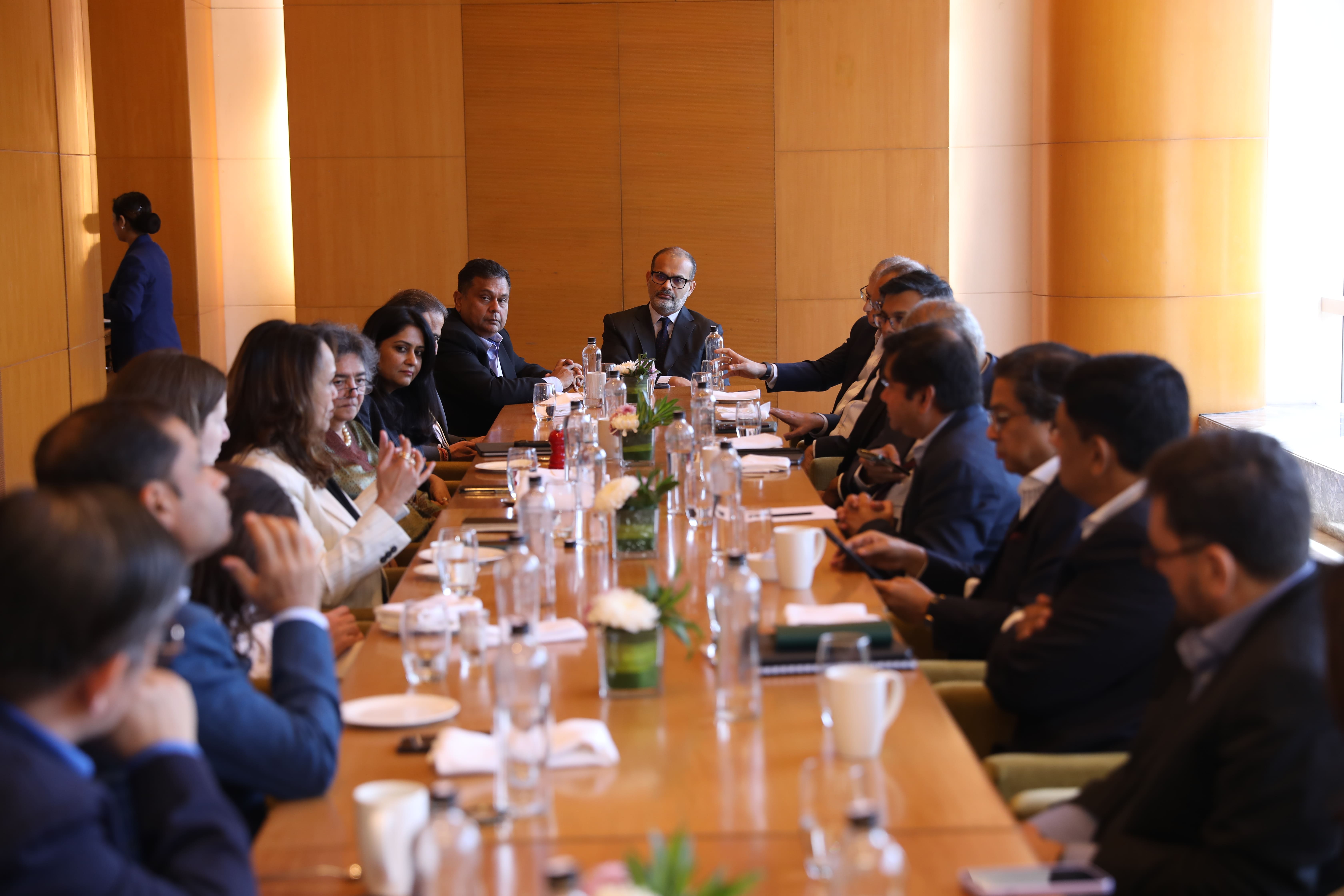 Businesspeople seated around a long table engaged in a meeting in a wood-paneled room.