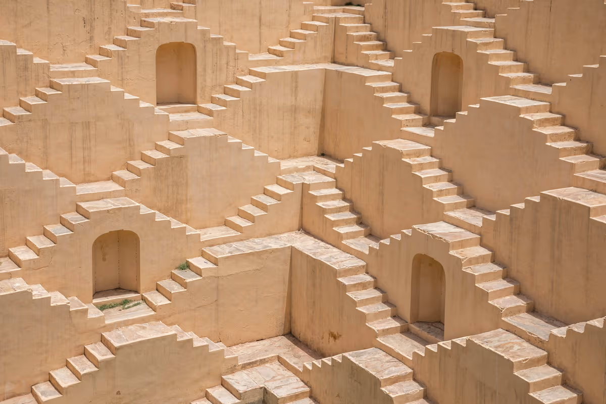 Patterned beige stone stairs forming geometric shapes with doorways in a stepwell structure.