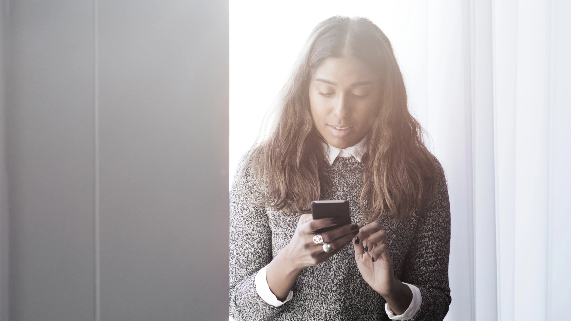 Kvinna tittar på sin mobiltelefon vid ett fönster.