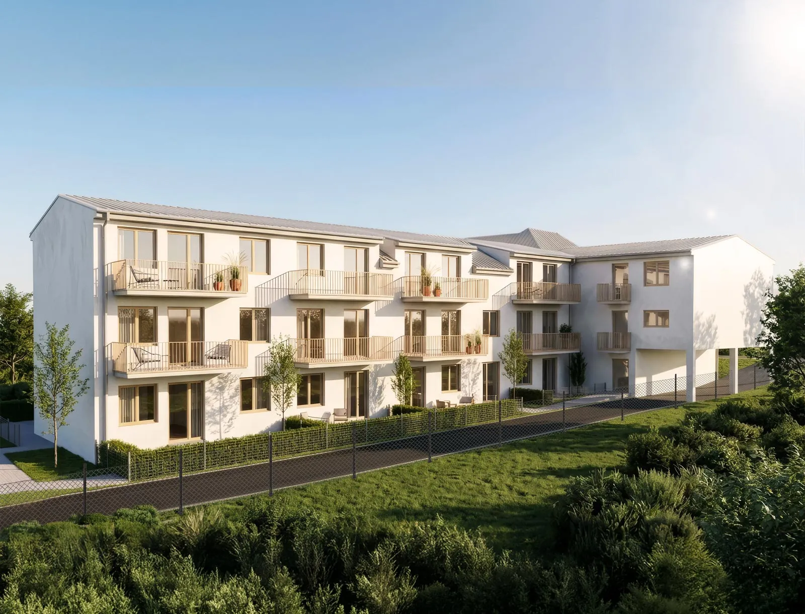 Modern three-story apartment building with balconies, outdoor seating, greenery, and clear sky.