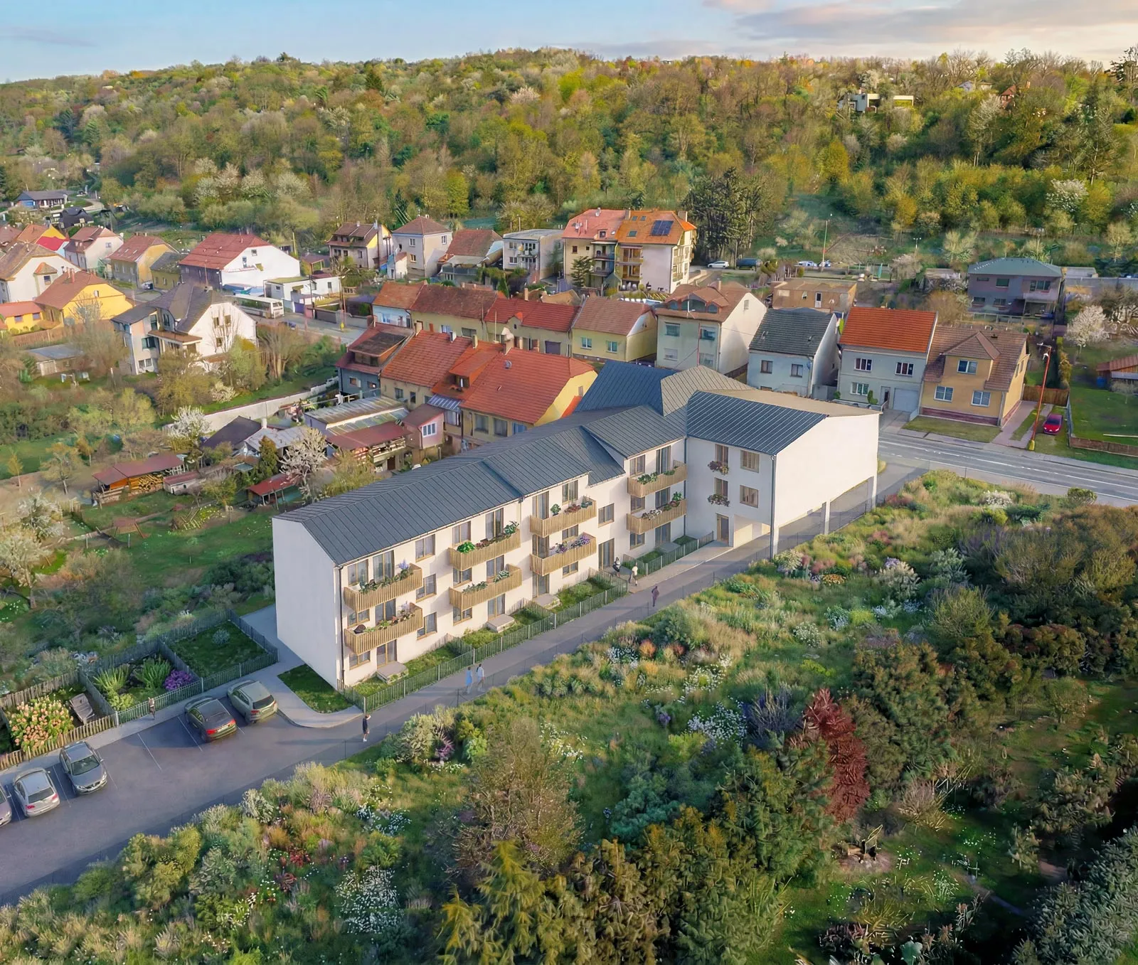 Aerial view of a modern apartment building with balconies next to residential houses and green wooded area.