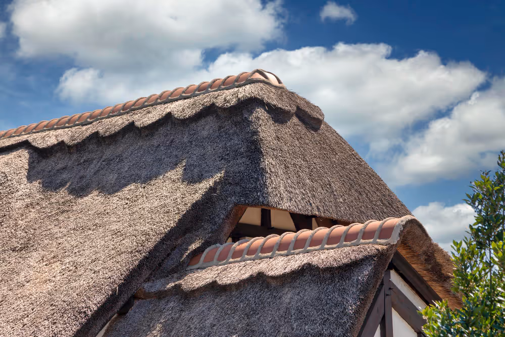 Nahaufnahme eines traditionellen Reetdachs mit Firstabdeckung und markanter Dachkonstruktion unter blauem Himmel.