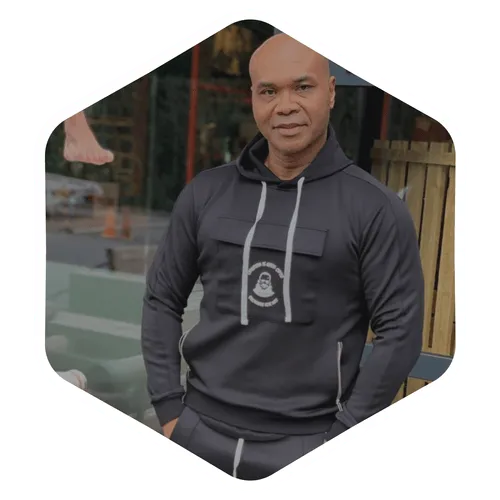 Oudere man in grijze hoodie staat buiten voor houten hek