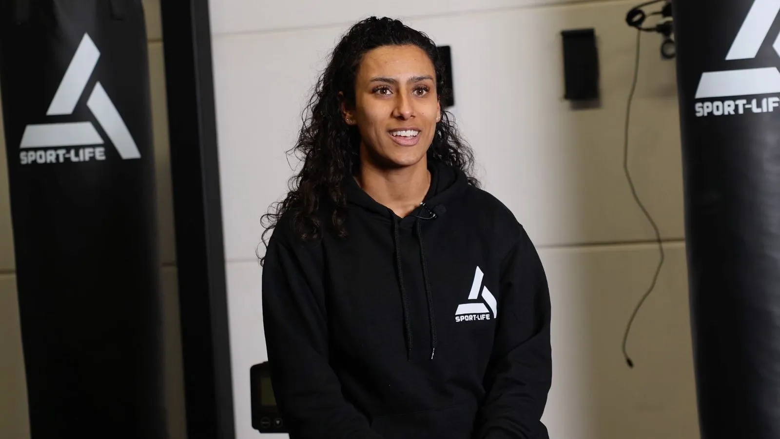 Glimlachende sporter in zwarte Sport-Life hoodie bij trainingsruimte