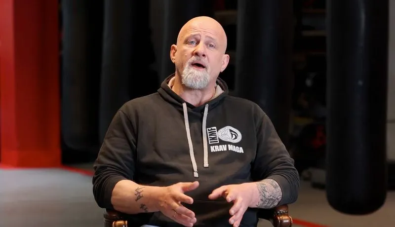 Kale man in Krav Maga hoodie geeft uitleg met handgebaren