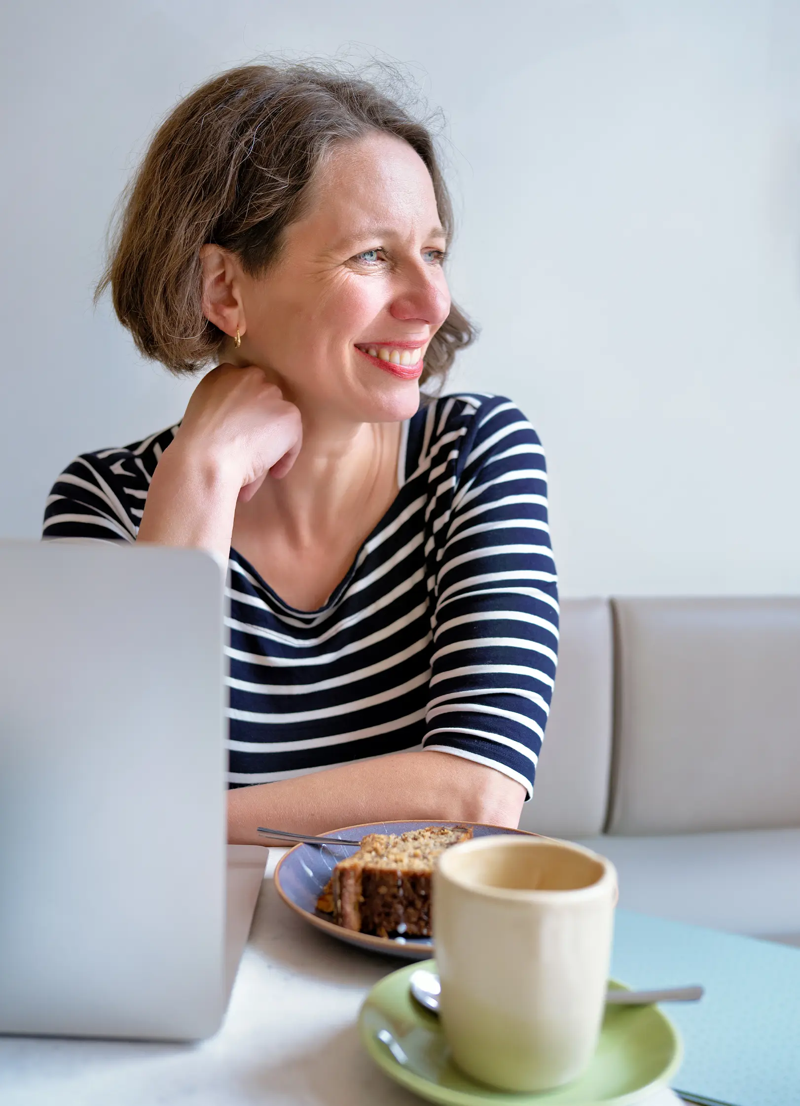 Blick hinter die Kulissen: Bärbel Becker sitzt mit Laptop, Kaffee und Kuchen in einem Berliner Café und schaut nachdenklich zur Seite