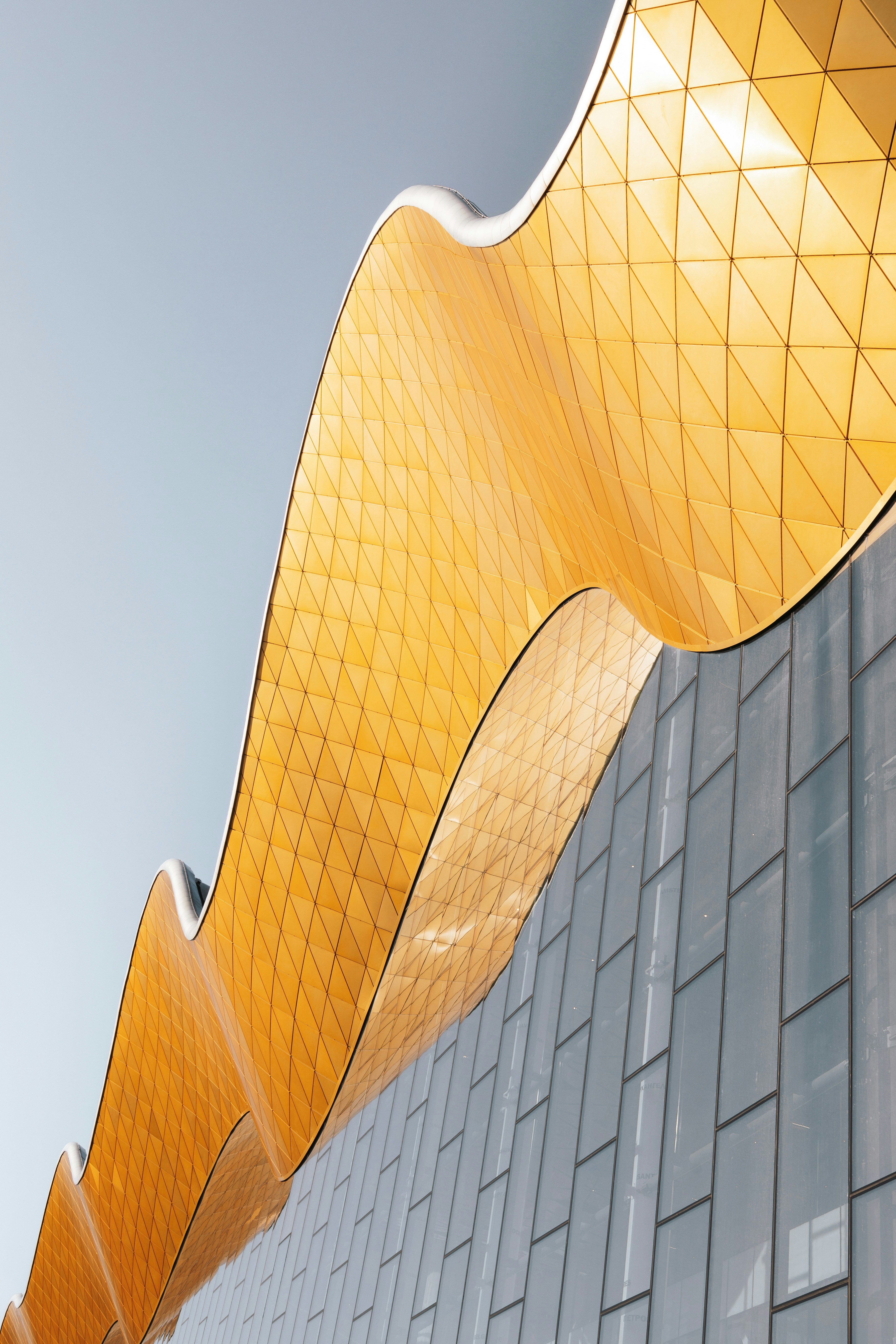 Modern building with a wavy golden roof and glass-paneled facade under clear sky.
