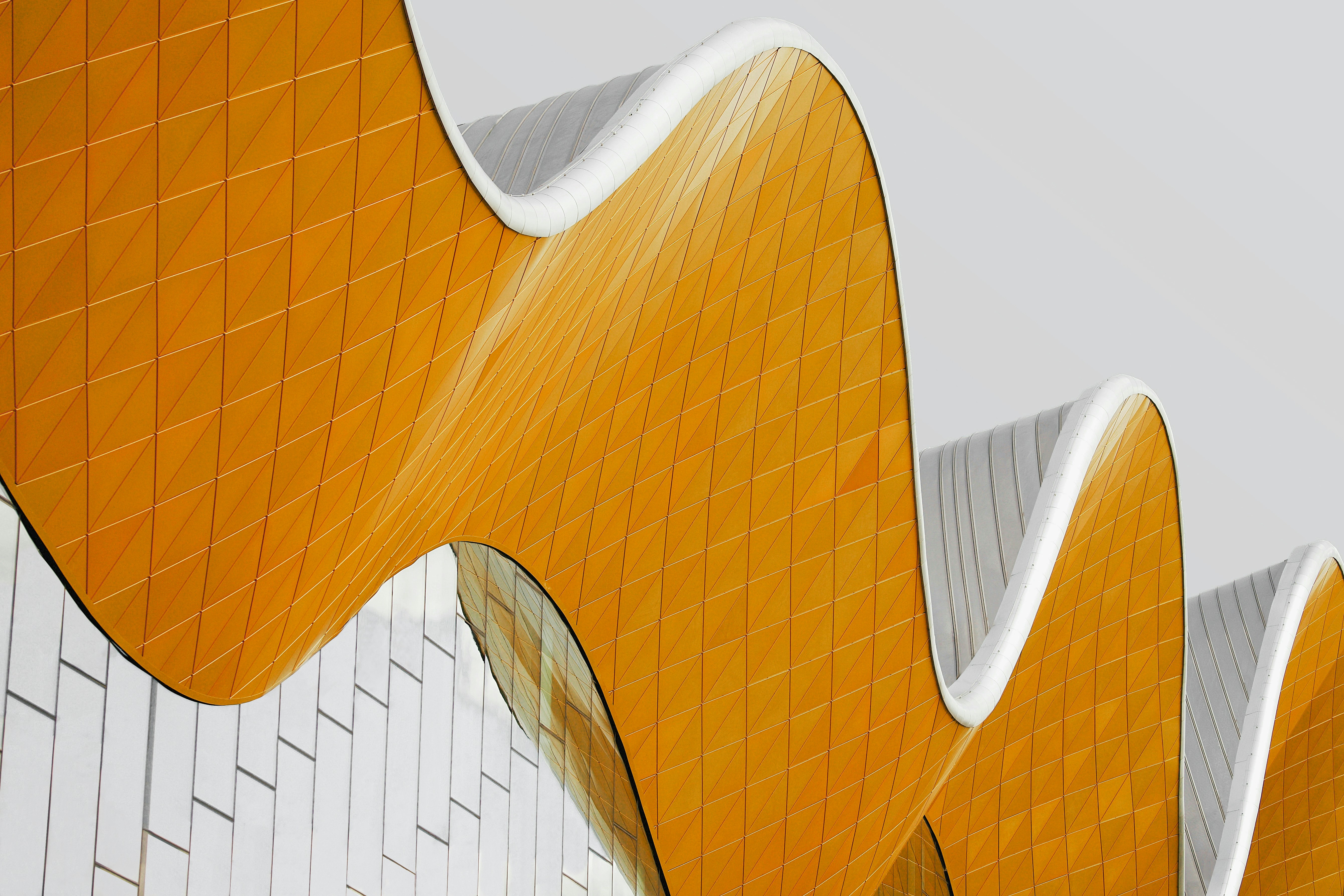 Curved architectural roof with yellow diamond-patterned tiles and white edges against a gray sky.