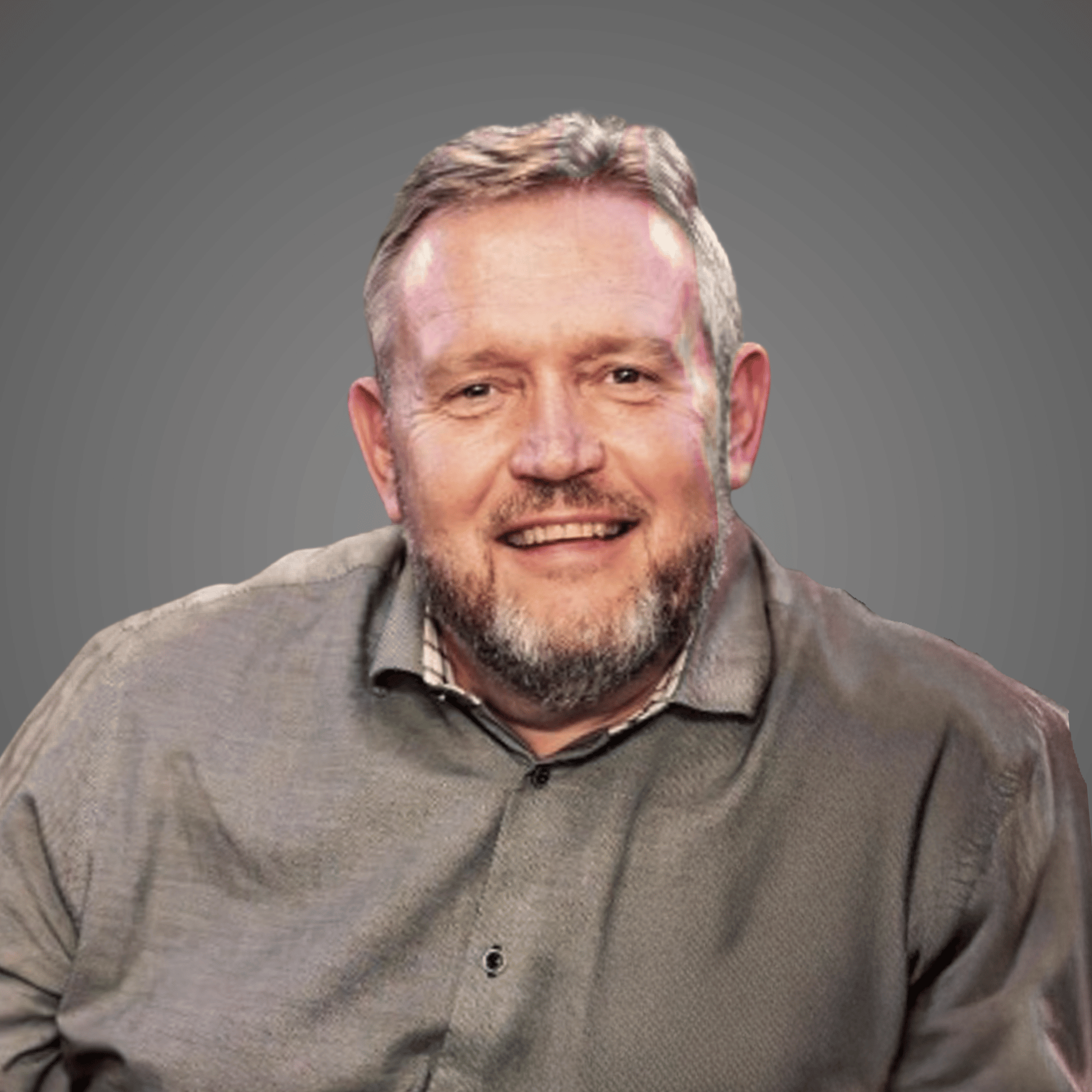 Smiling middle-aged man with beard wearing a gray button-up shirt against a gray background.