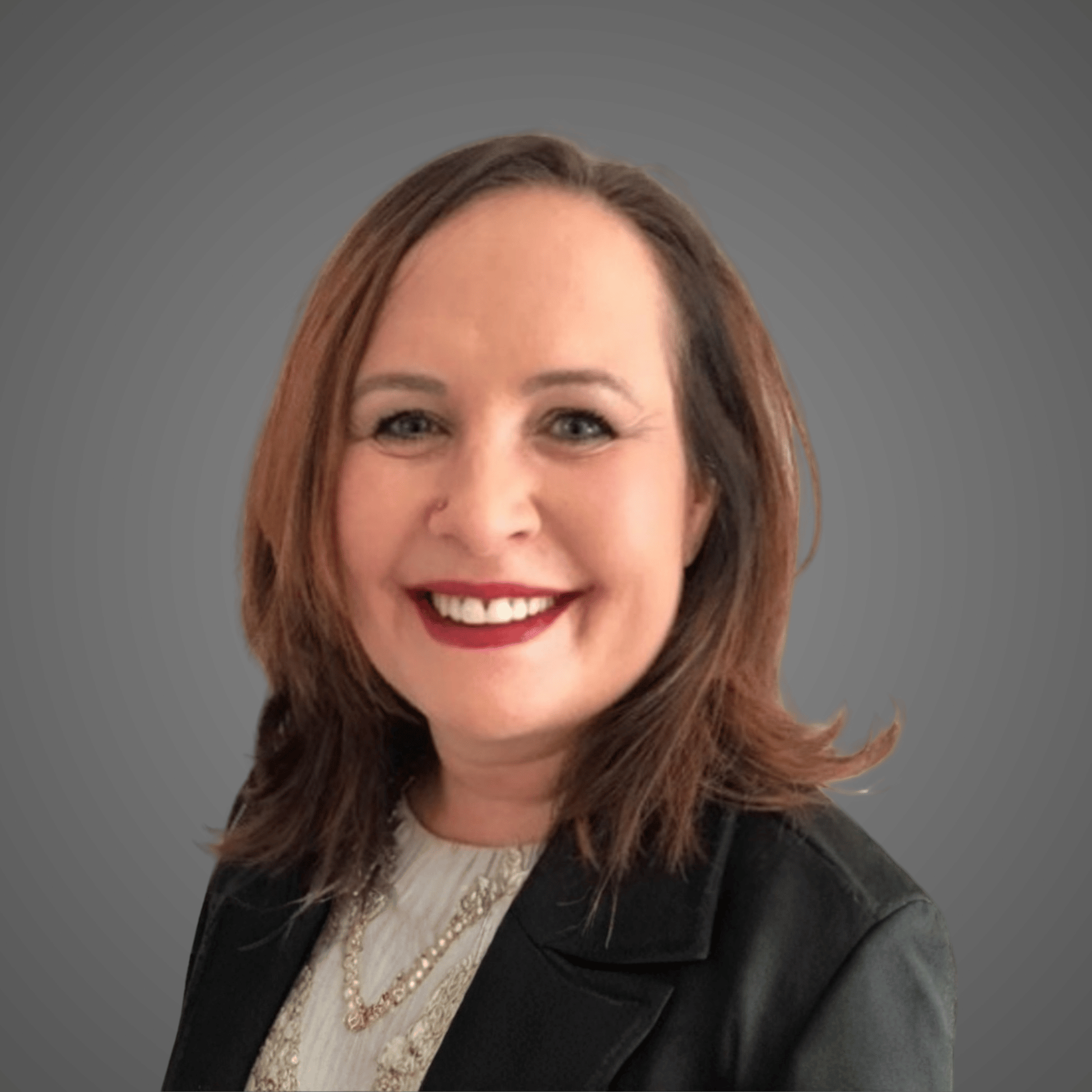 Smiling woman with shoulder-length brown hair wearing a black blazer and layered necklaces.