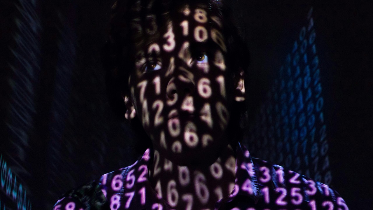 Person’s face and shirt covered in projected glowing numbers in a dark setting.