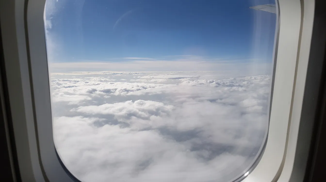 The image captures a serene view from an airplane window, showcasing fluffy white clouds against a vibrant blue sky during a calm flight. This peaceful scene highlights the beauty of flying and the vastness of the airspace above.