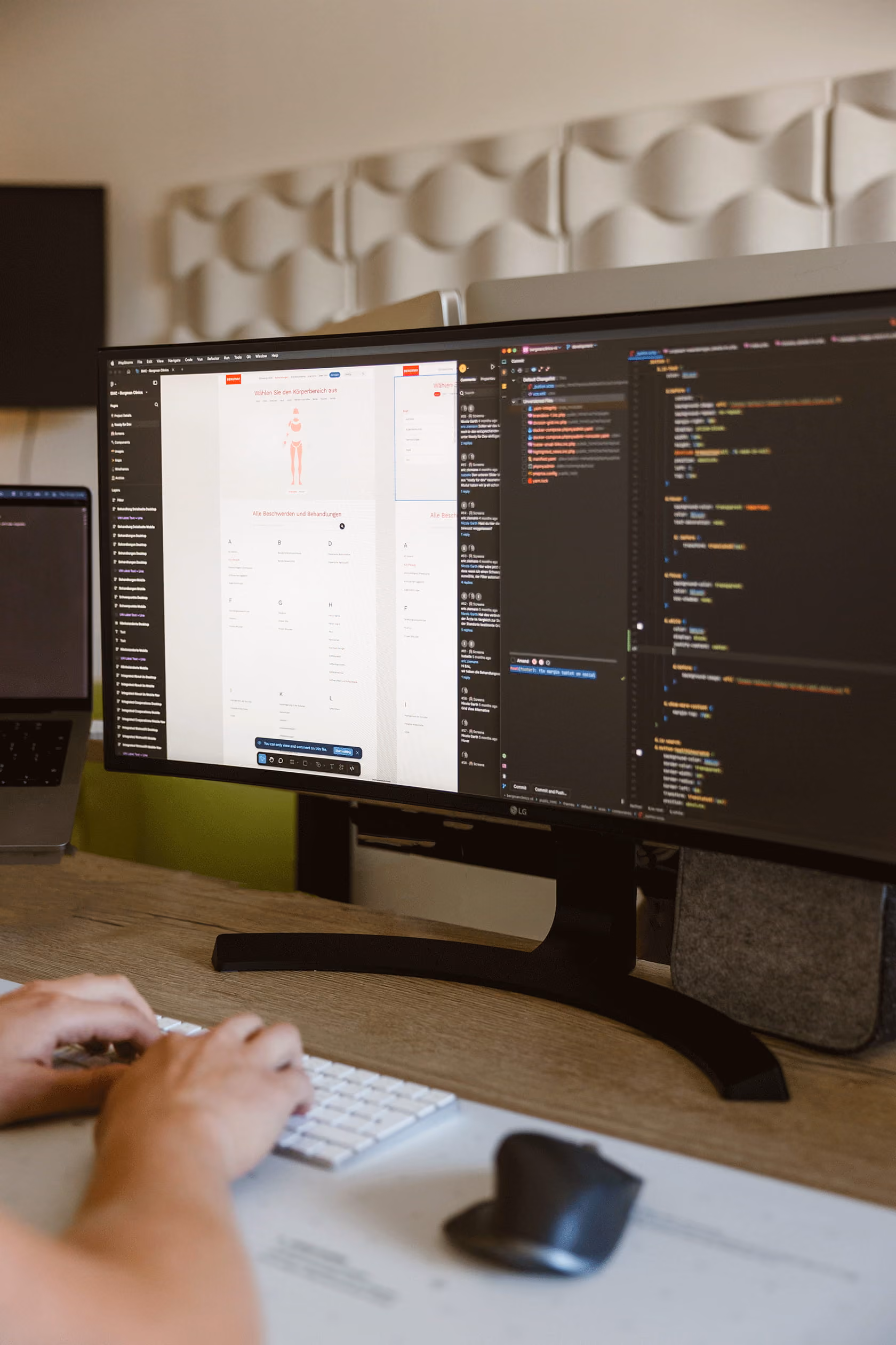 Een persoon typt op een toetsenbord voor een brede monitor met code en een ontwerpinterface.