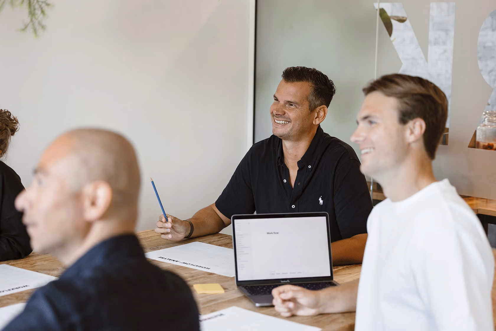 Mensen in een vergadering rond een tafel met notities en een laptop.