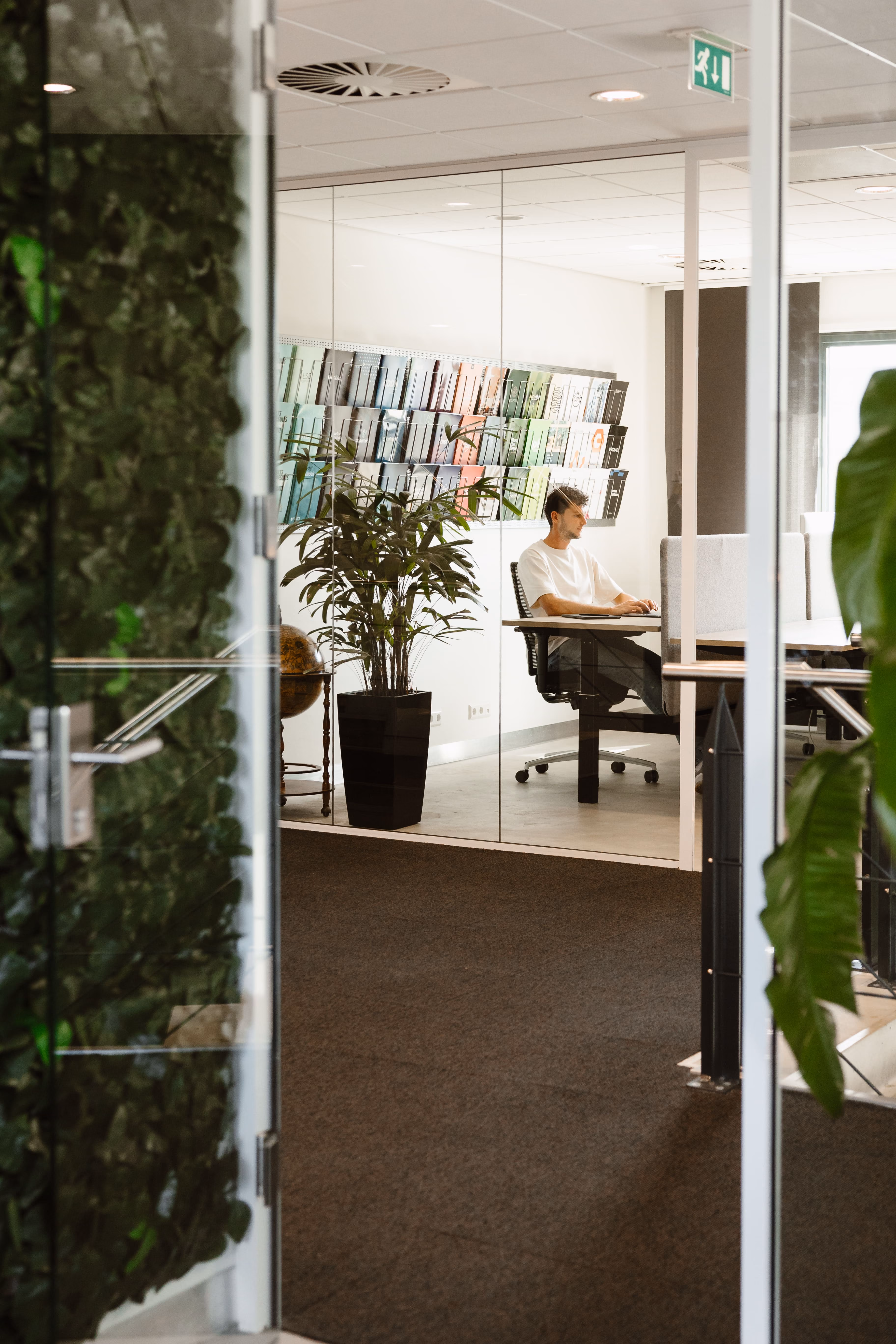 Man werkt op laptop in een modern kantoor met glazen muren en groene planten.