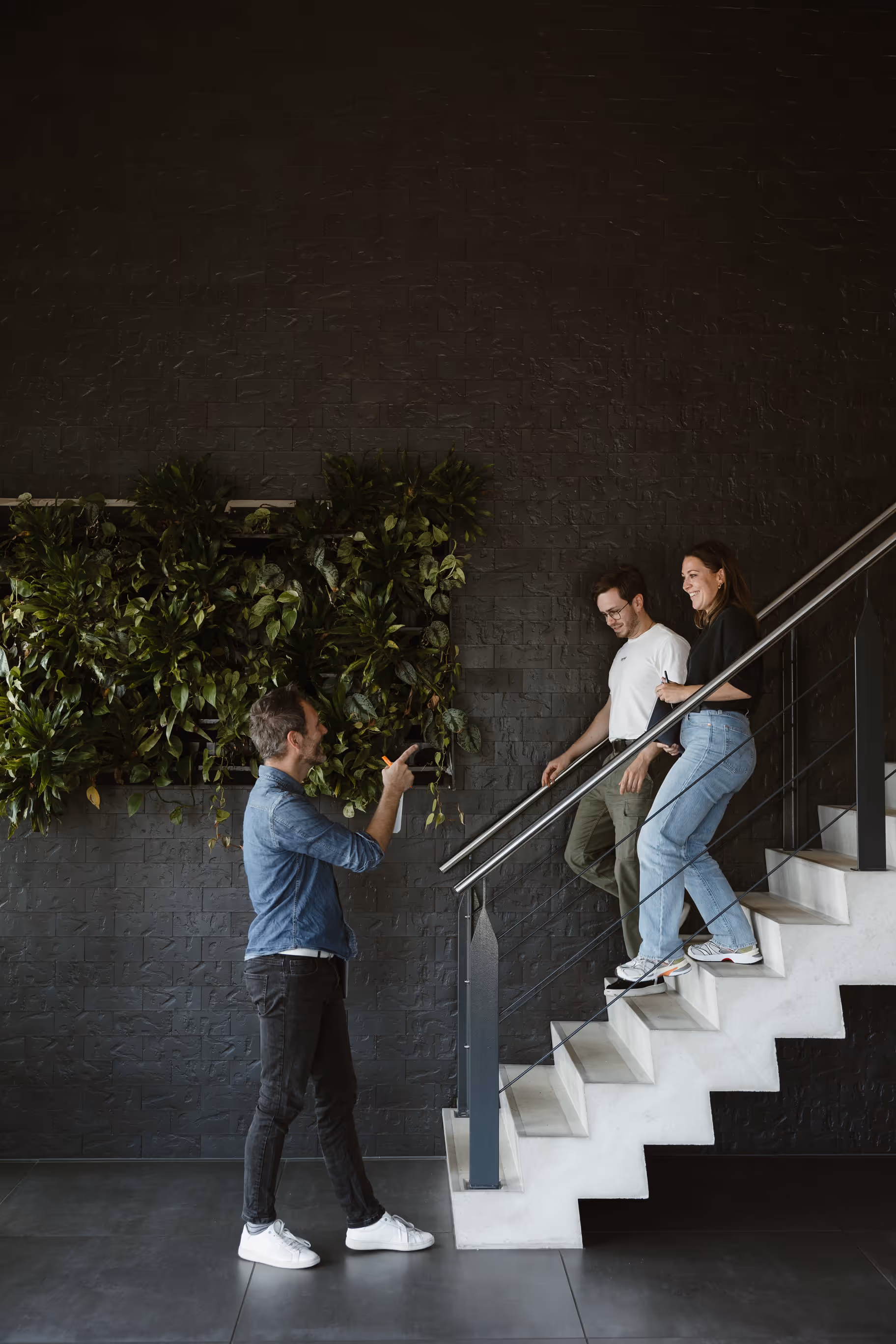 Man maakt foto van man en vrouw die samen de trap aflopen in een modern interieur met groene muur.
