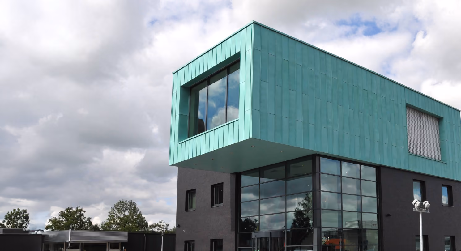 Modern gebouw met een opvallend groen bovenste verdieping en grote glazen gevel onder bewolkte lucht.