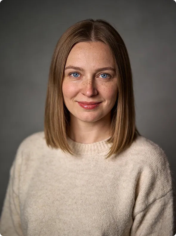 Woman with straight light brown hair, blue eyes, freckles, and beige sweater smiles at the camera.