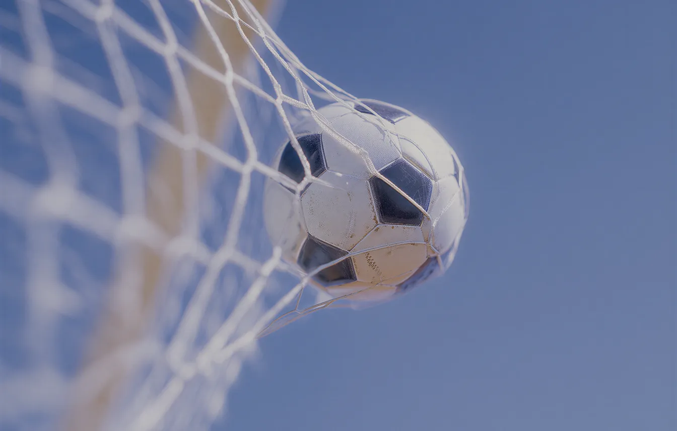 Black and white soccer ball caught in a white net against a blue sky.