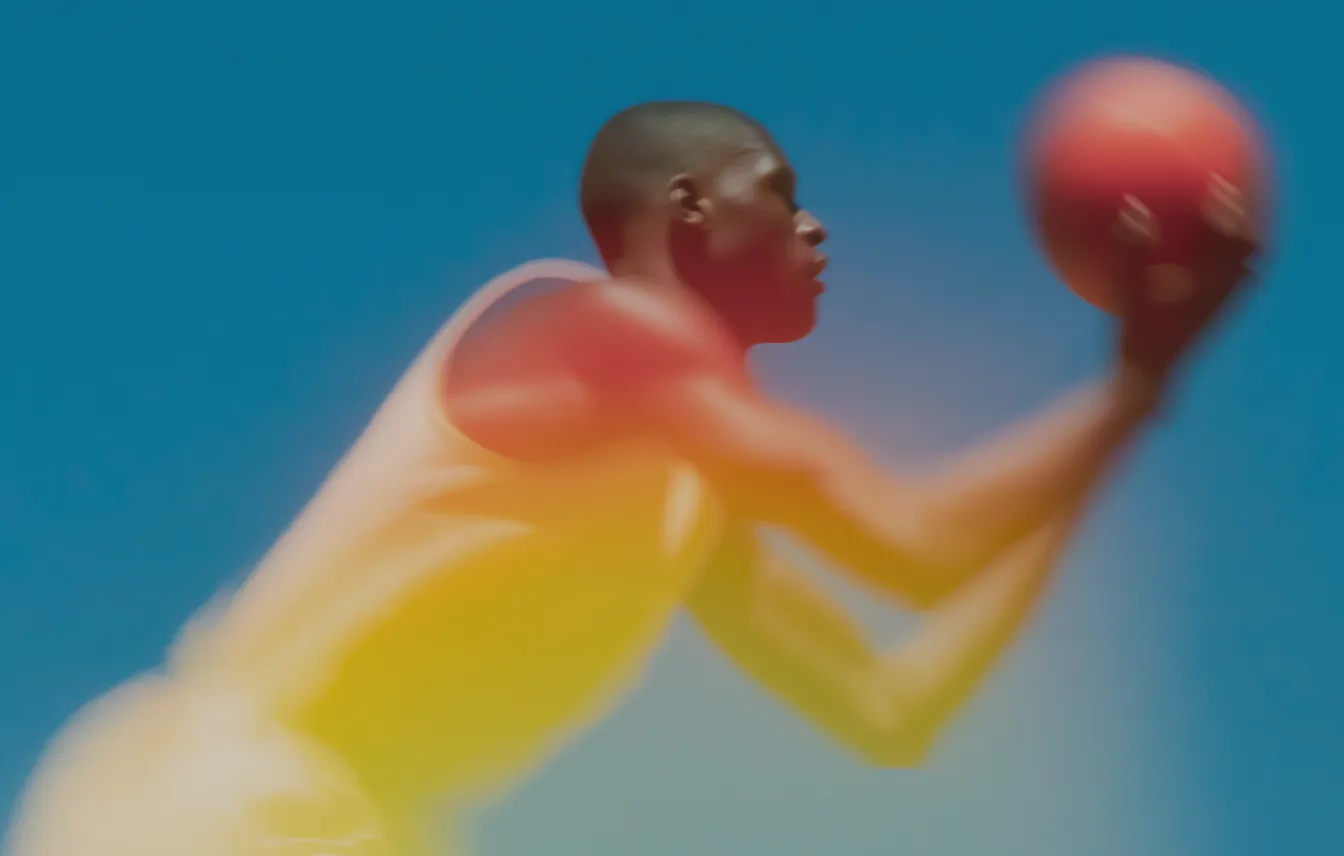 Blurred image of a man in a white tank top preparing to shoot a basketball against a blue sky.