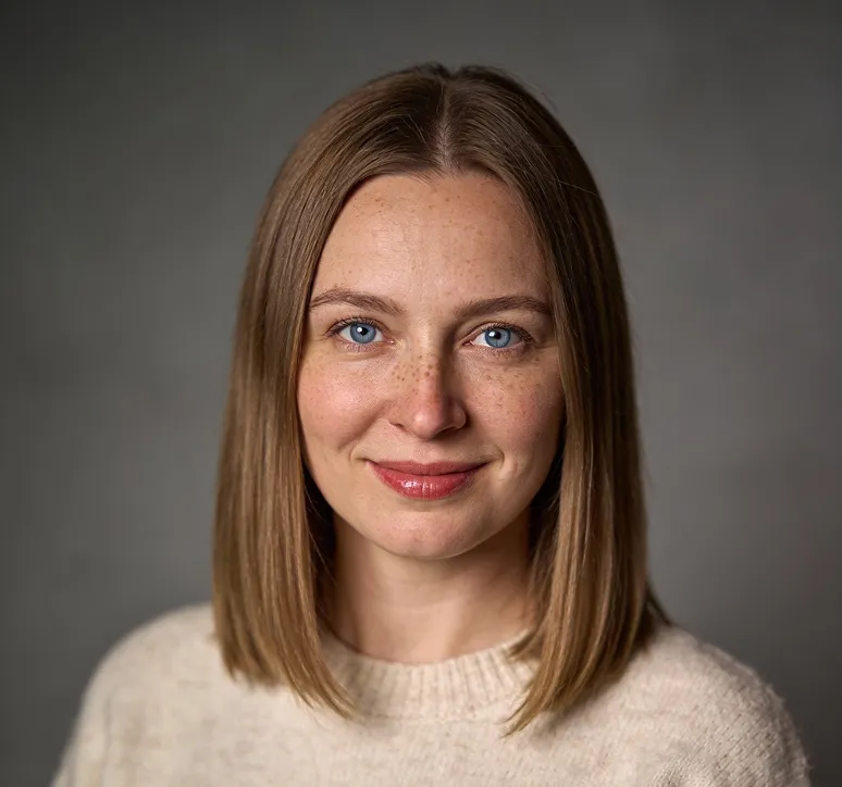 Smiling woman with blue eyes, freckles, and straight shoulder-length light brown hair wearing a beige sweater.