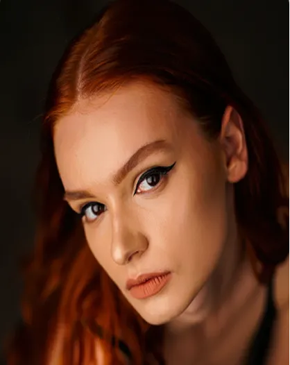 Close-up of a red-haired woman with winged eyeliner and neutral lipstick looking at the camera.