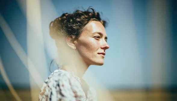 Profile of a woman with curly hair looking into the distance against a blurred outdoor background.
