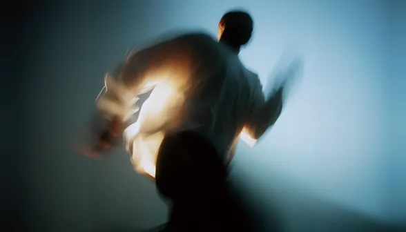 Blurred silhouette of a person in motion with bright light behind them against a blue gradient background.