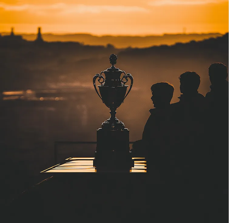 Silhouetted trophy and three people against a golden sunset background.