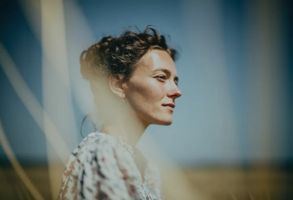 Profile of a woman with curly hair looking into the distance with a blurred natural background.