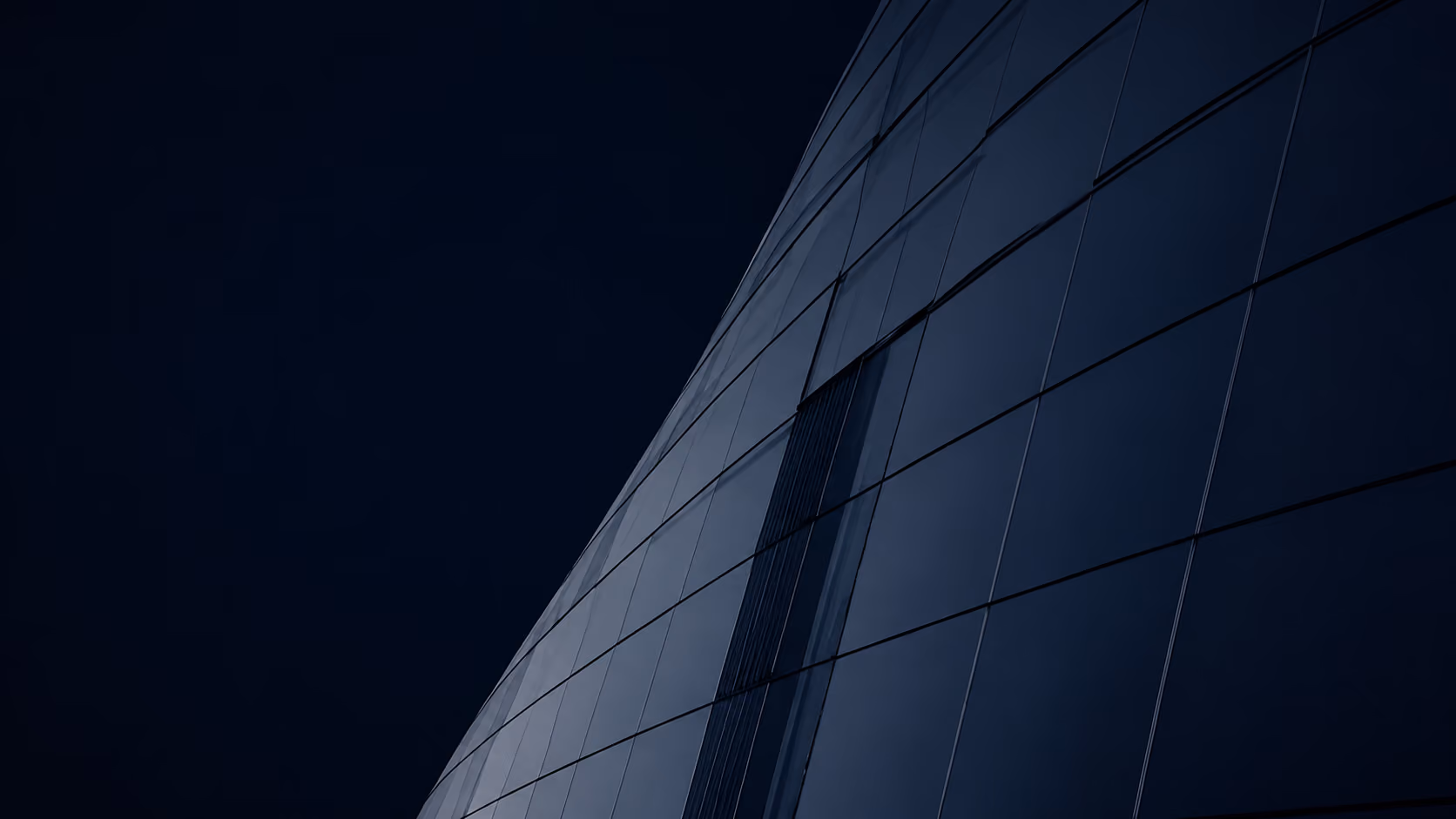 Curved dark glass facade of modern building against a night sky.