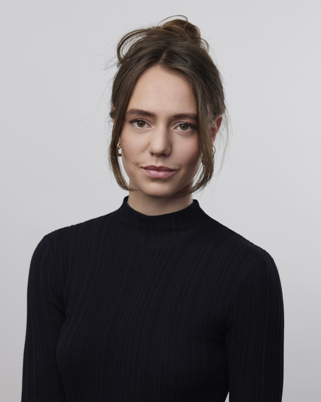 Portrait d'une femme aux cheveux bruns relevés portant un pull noir à col montant.