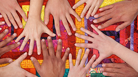 A diverse group of people place their hands together on a colorful background.