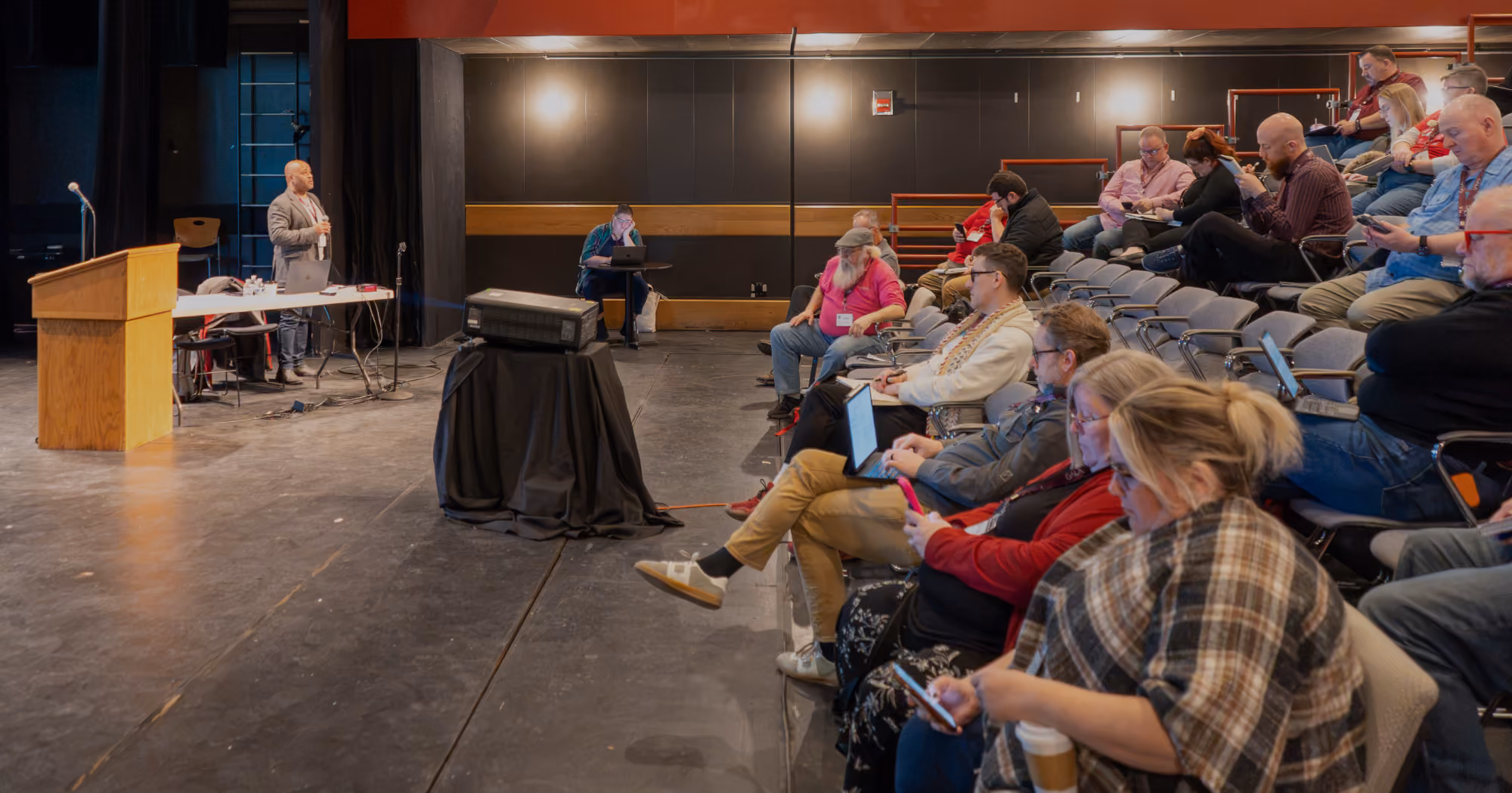 A presenter stands in front of an audience of note-taking attendees at Symposium 2026.