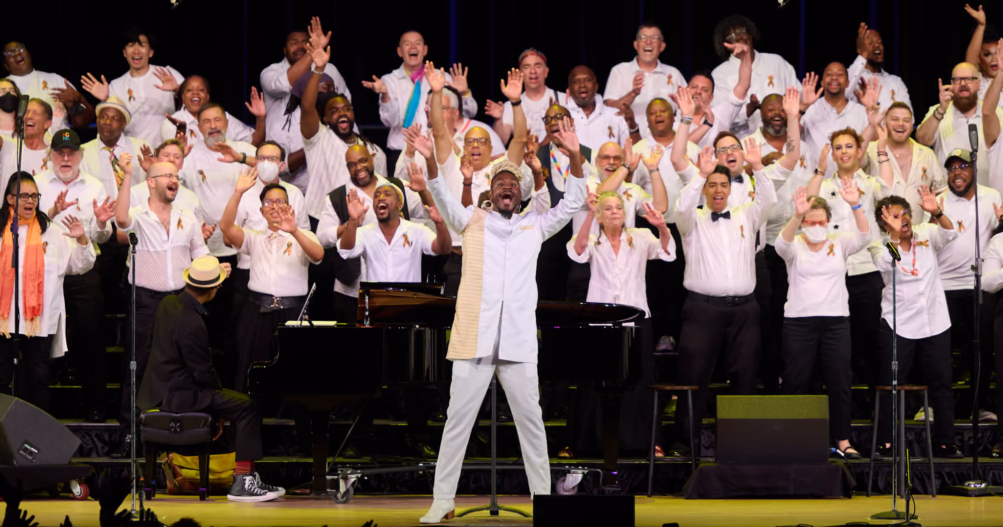 The Queer Gospel Choir at GALA Festival 2024 face the audience with their conductor enthusiastically sing while waving their hands in the air