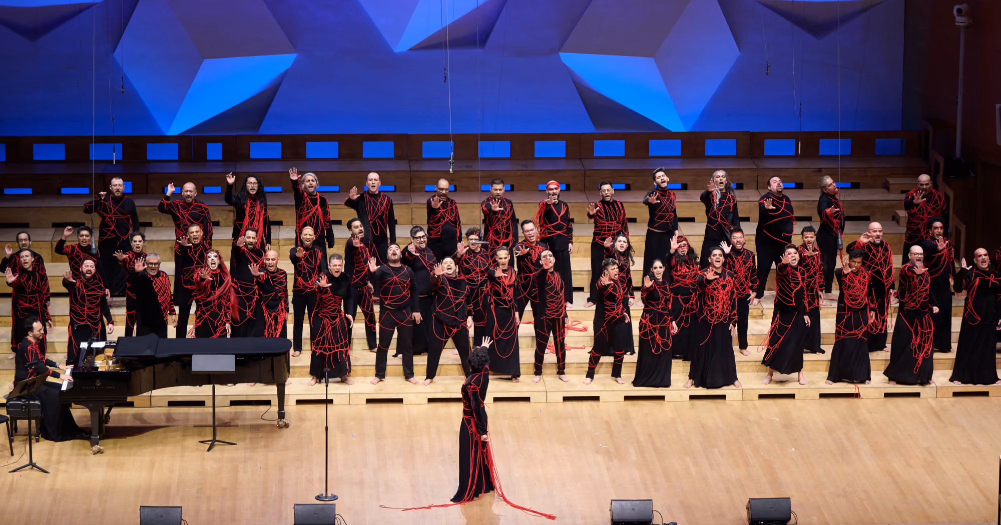 The Voces Latinas Festival Chorus at GALA Choruses Festival 2024 are spread across the stage thrusting their right arms forward imploringly mid-song.