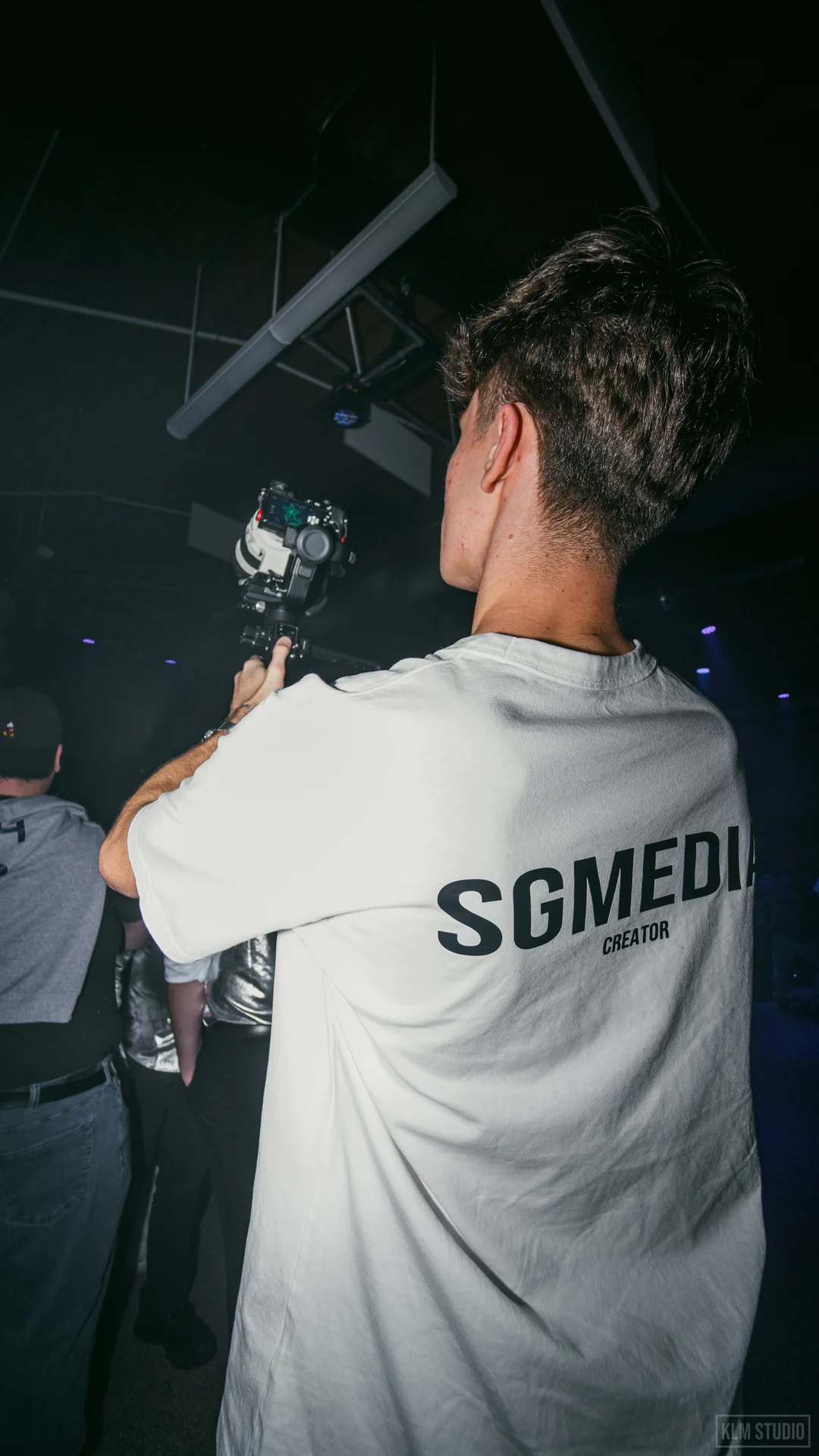 Two men having an interview near a railing inside an arcade with cameras and a cameraman recording.