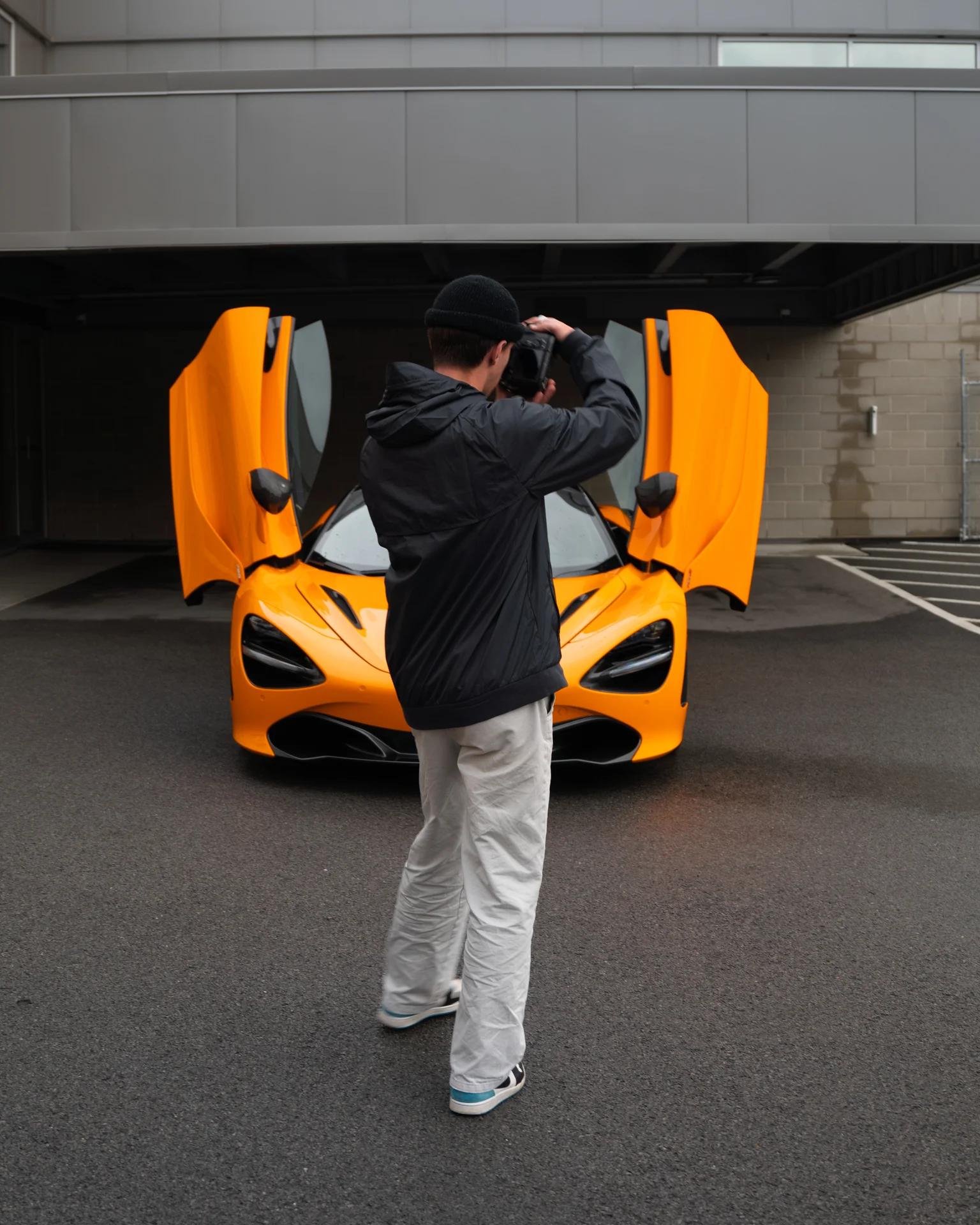 Photographer taking a picture of an orange sports car with butterfly doors open.